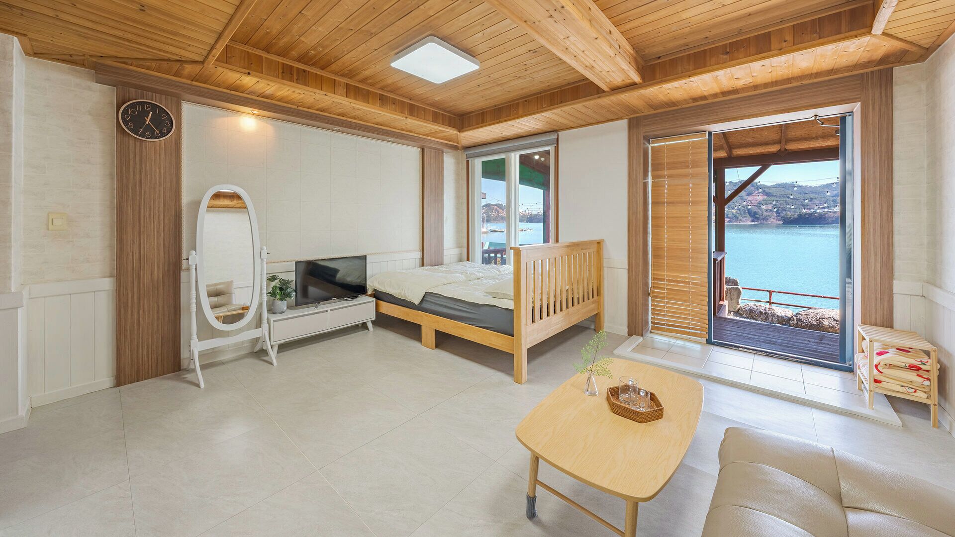 Una habitación con cama, televisor, mesa de madera y vista al mar por un ventanal corredero.