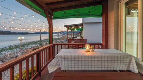 A covered outdoor seating area with a table and chairs, overlooking a body of water.
