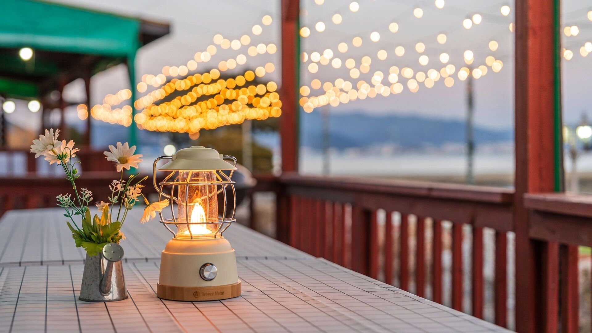 A table with a lantern, flowers, and string lights.