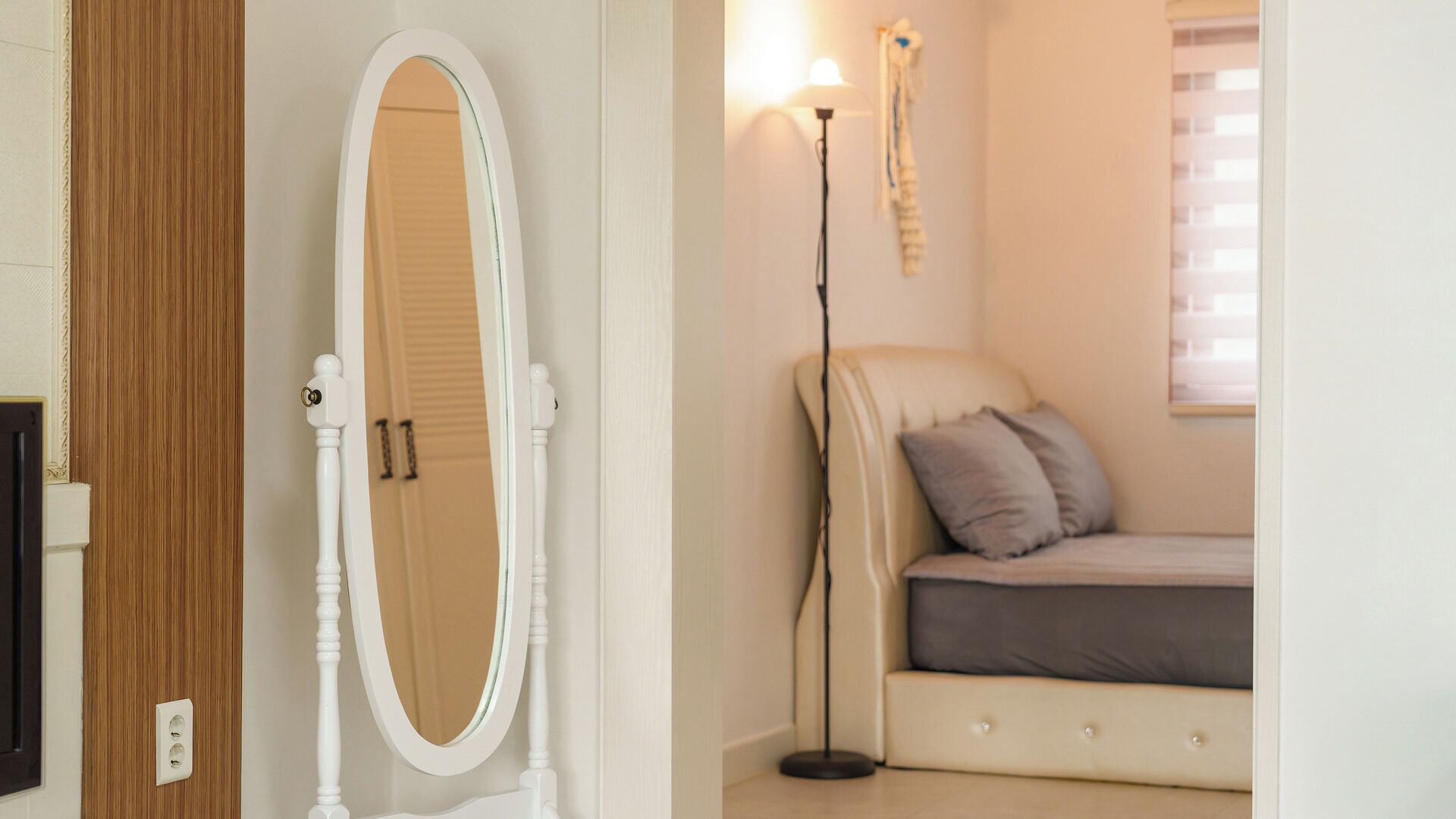 Quarto com penteadeira branca, mesa de cabeceira, luminária e janela com persianas.