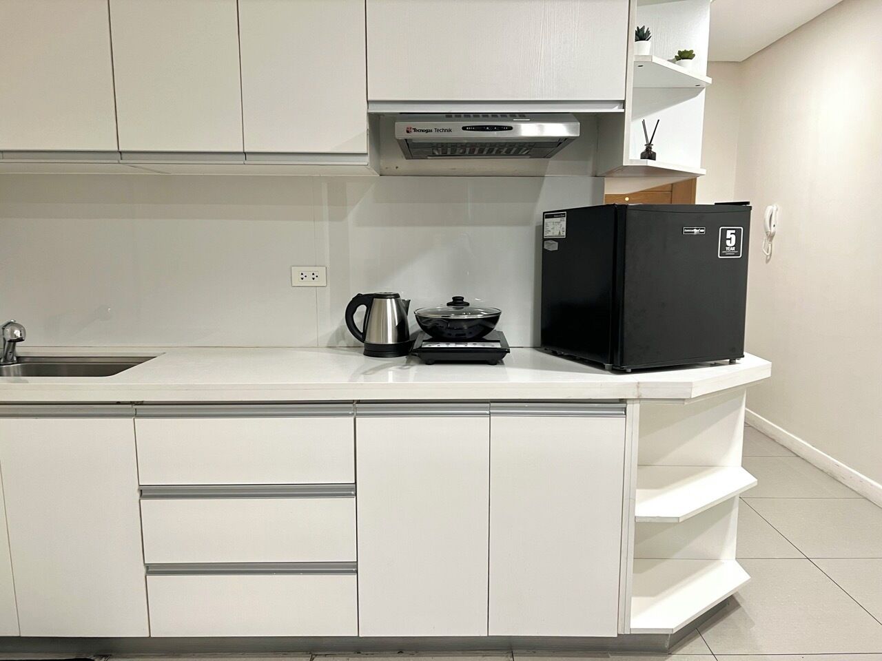 A modern kitchen with white cabinetry, a black refrigerator, a kettle, and a stove.