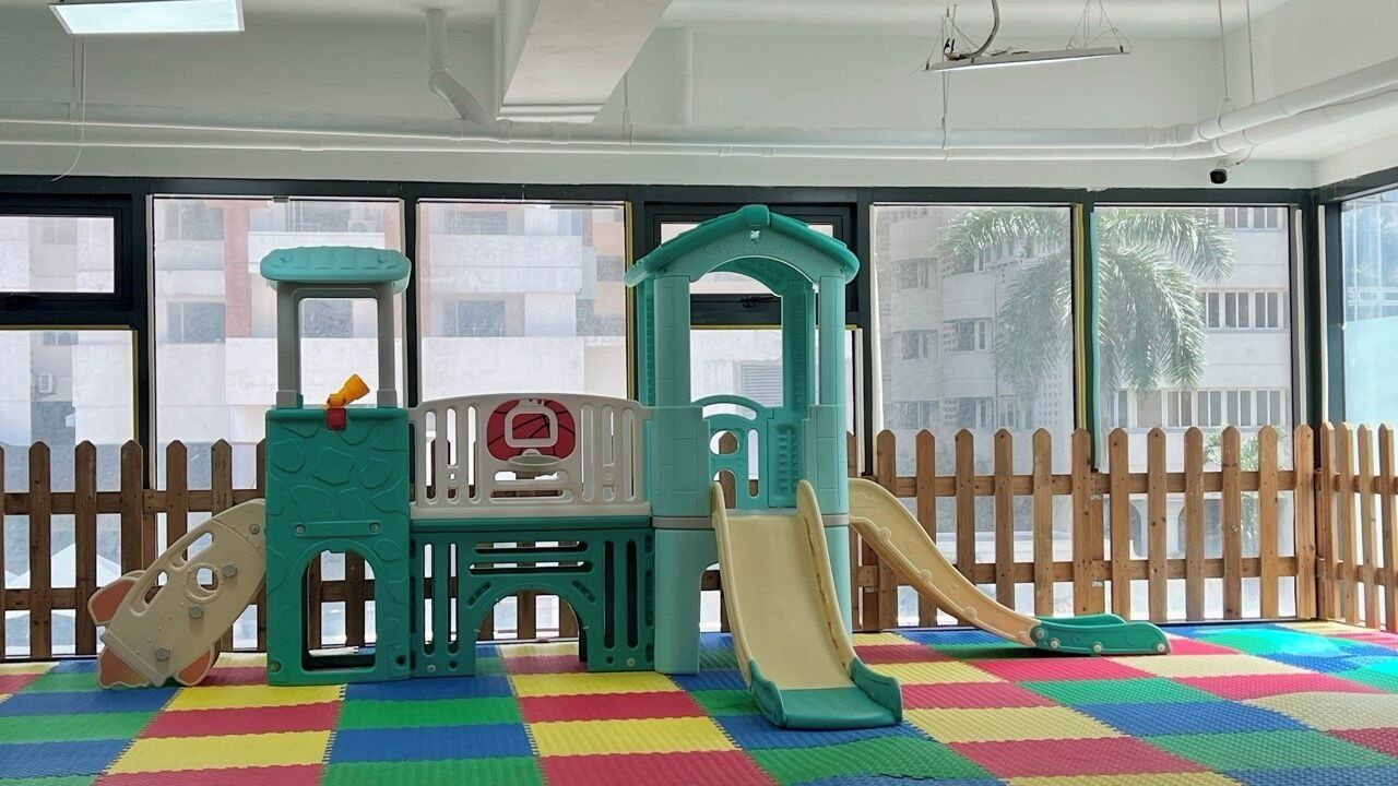 A children's play area with a slide and climbing structures, a wooden fence outside, and a colorful play mat.