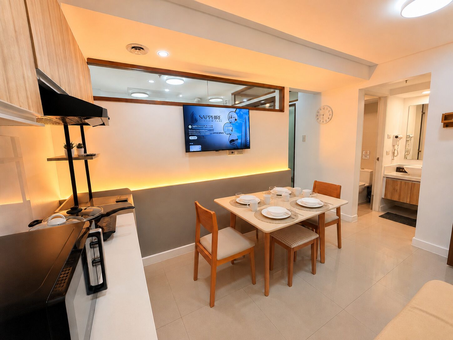 Una cocina moderna con comedor, televisor de pantalla plana sobre la encimera y un reloj a la vista en la pared.