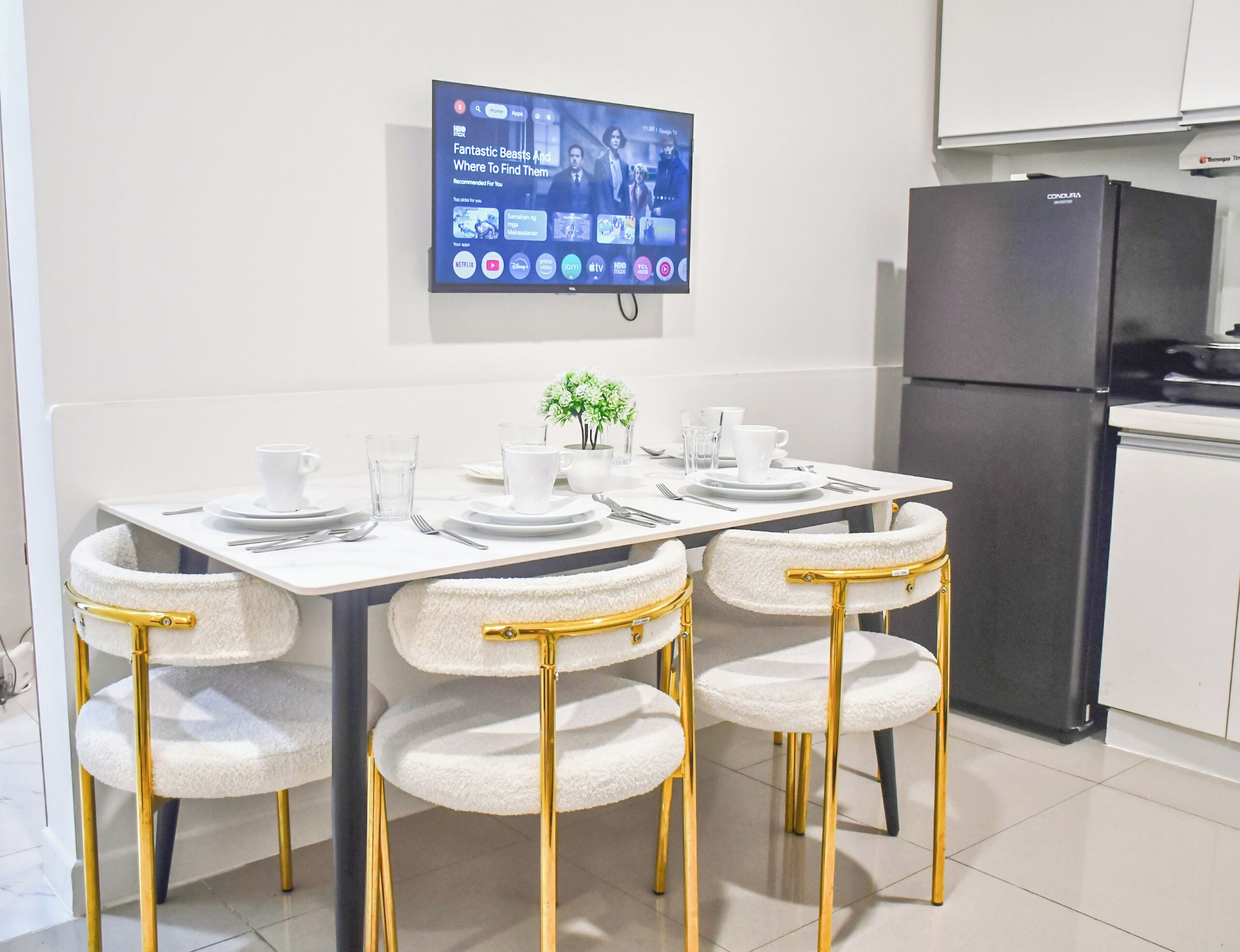A modern kitchen with a dining table set for four, a black refrigerator, and a mounted television displaying a streaming service interface.