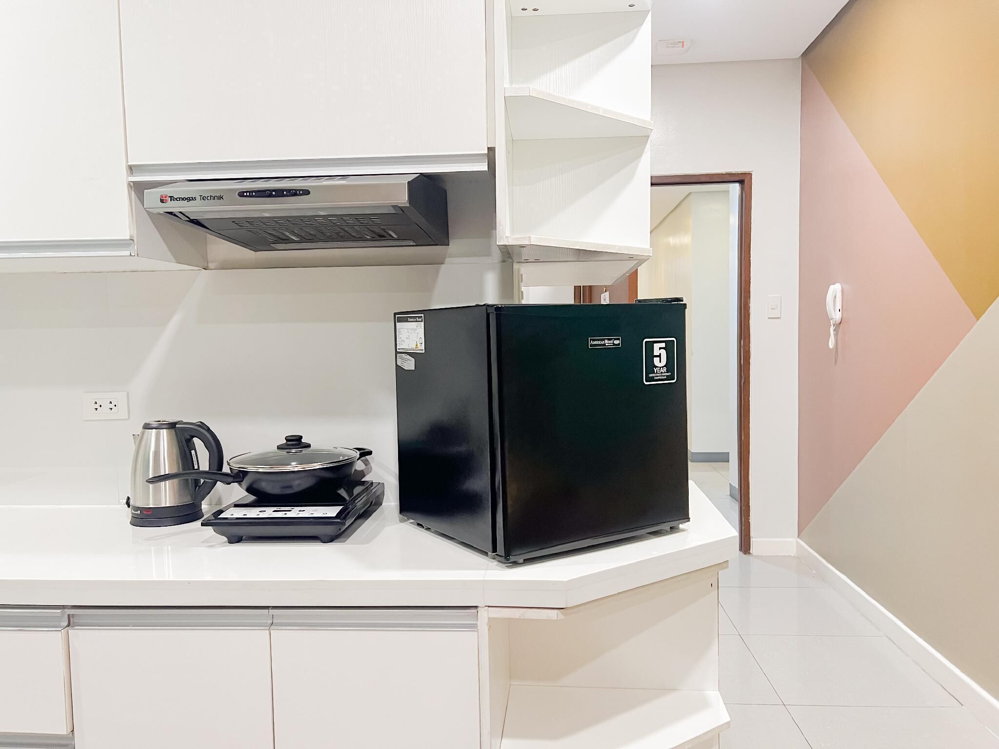 A compact kitchenette with a black refrigerator, a kettle, and a stove.