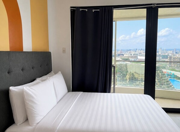Habitación de hotel con una cama grande y vistas a un paisaje urbano desde un balcón.