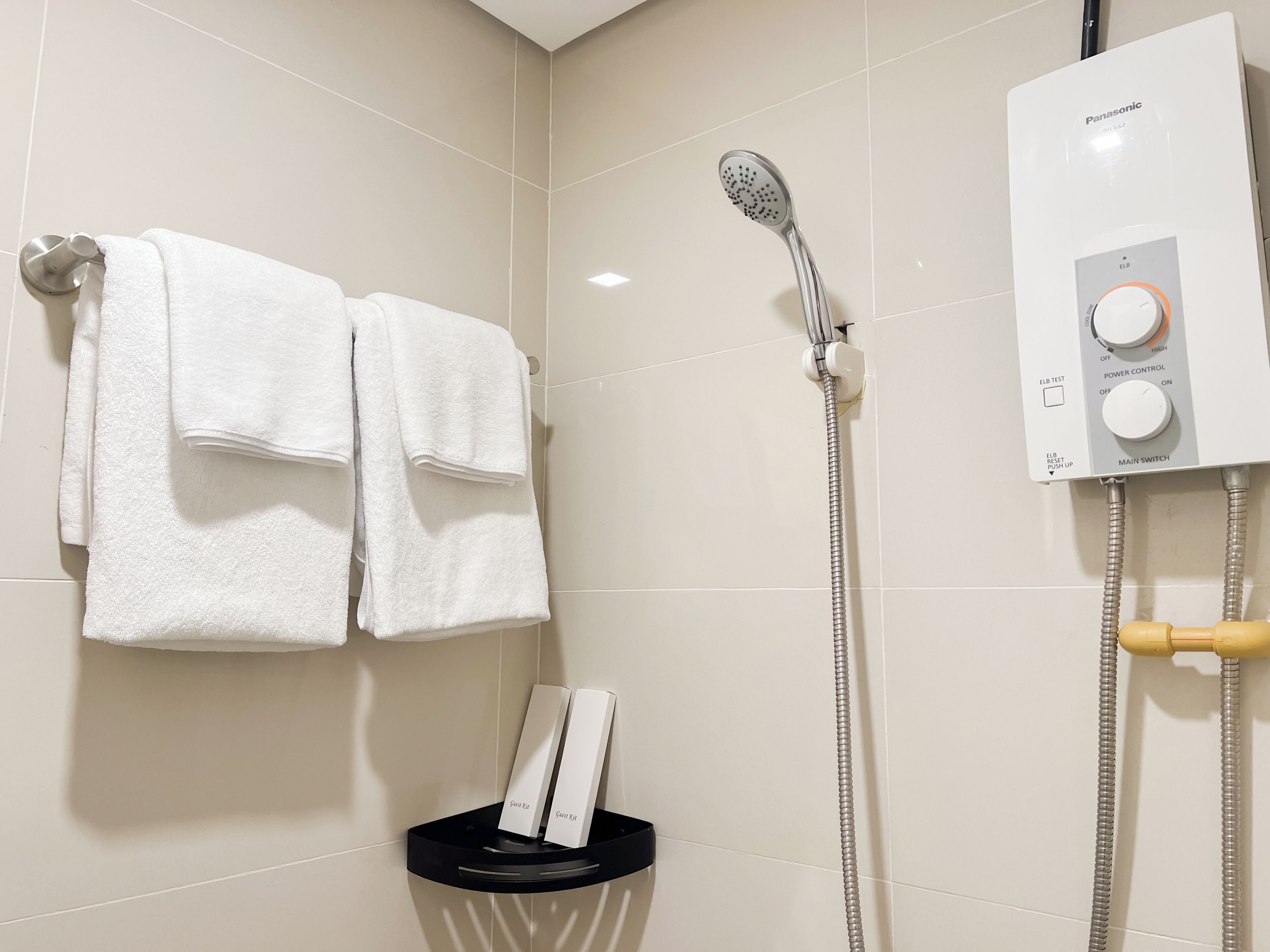 A bathroom with a shower, a towel rack with two towels, a soap dispenser, and a water heater control panel.