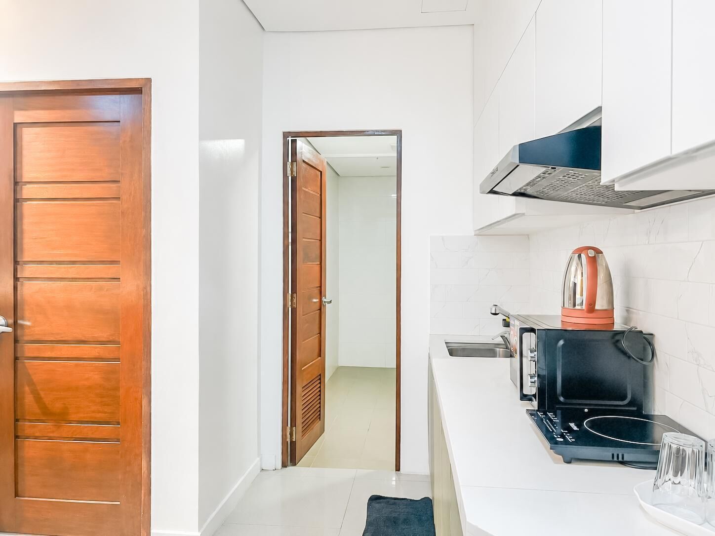 Cocina compacta con puerta de madera, microondas, hervidor y una pequeña encimera.