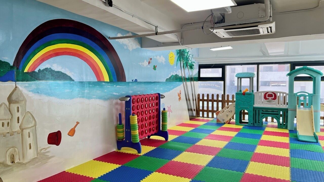 Une salle de jeux avec un sol coloré, un château, une fresque représentant un arc-en-ciel et des structures de jeu.