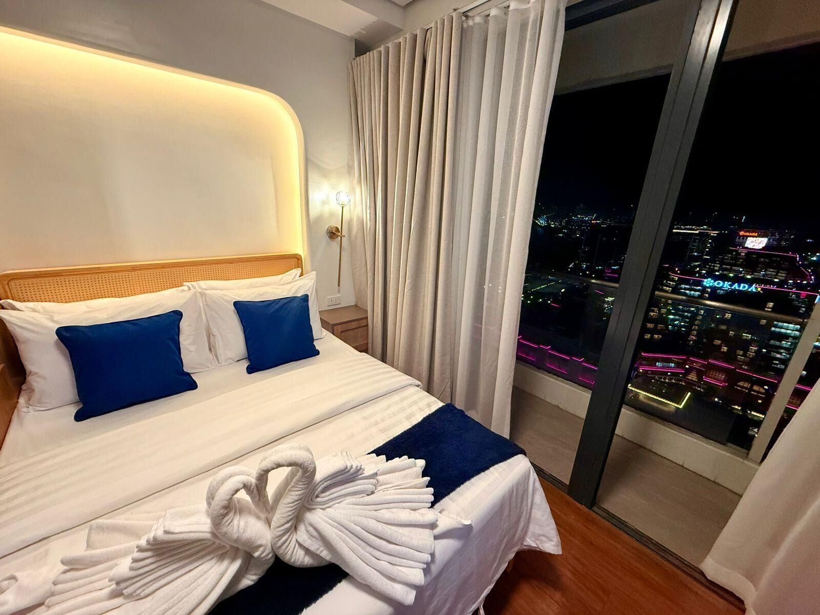 A hotel room with a bed, a view of a cityscape, and a window with curtains.
