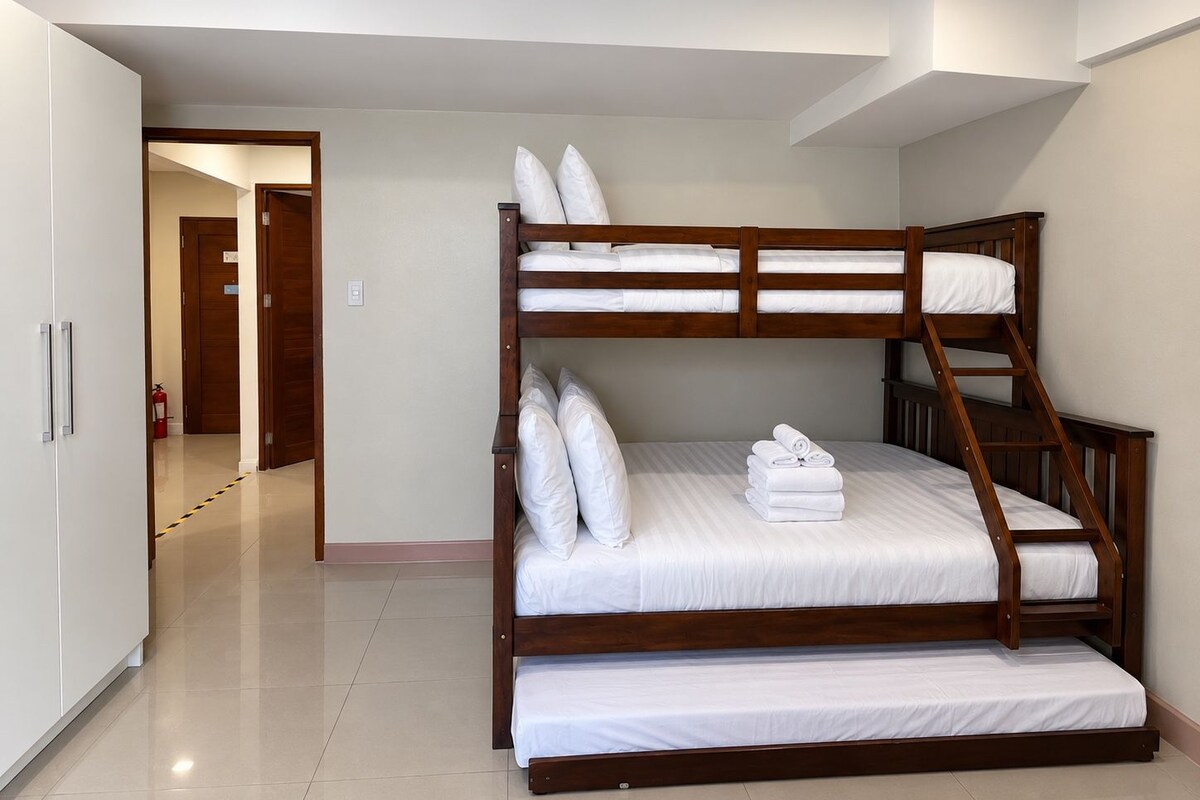 A bunk bed with white bedding in a room with a tiled floor and a door in the background.