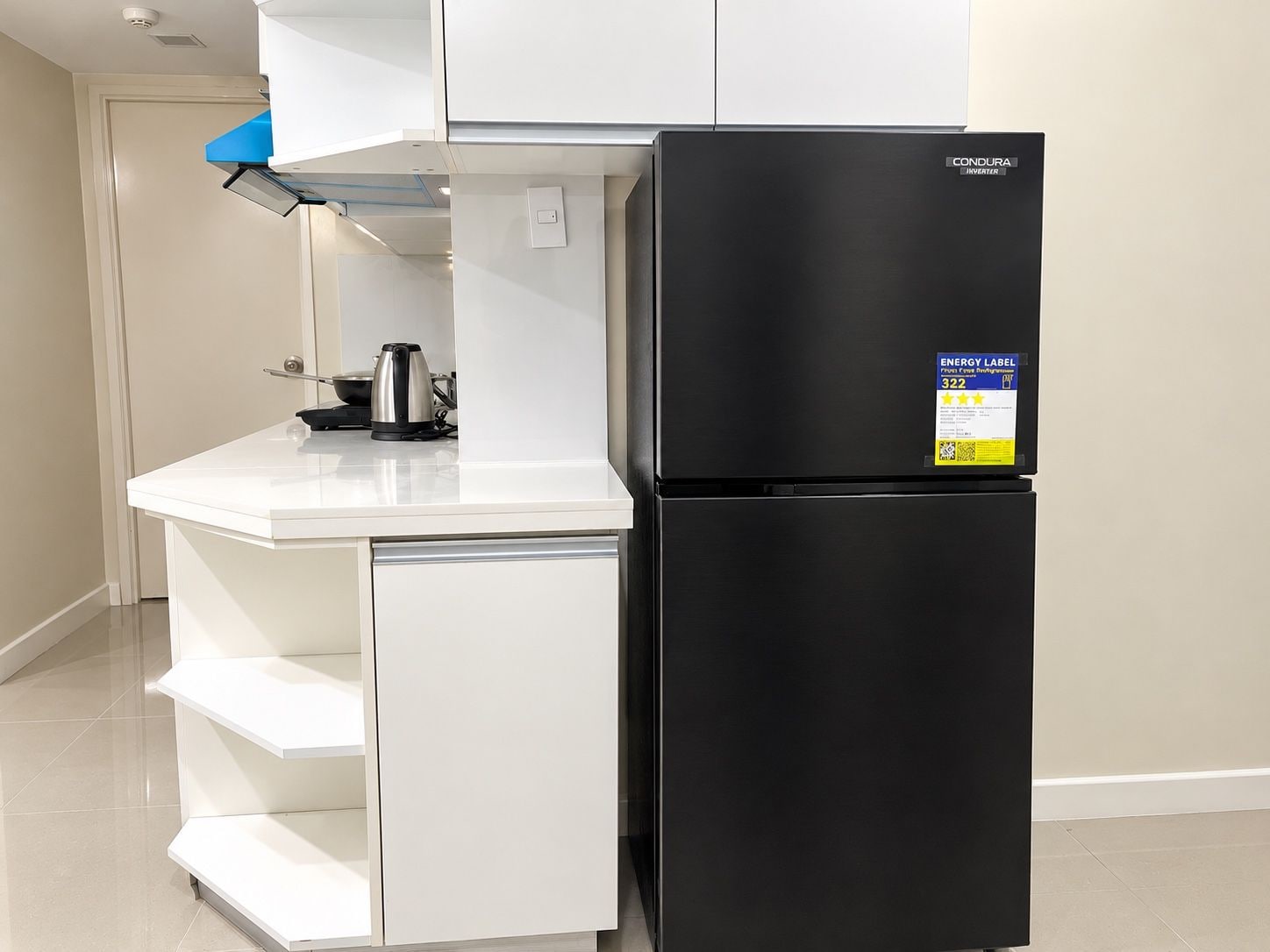 A compact kitchen with a black refrigerator, a white countertop, and a kettle.