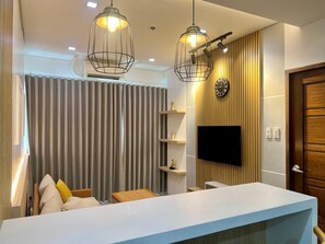 A modern living room with a white sofa, a TV mounted on the wall, and pendant lighting. - Sapphire Seaview Park (Parañaque)