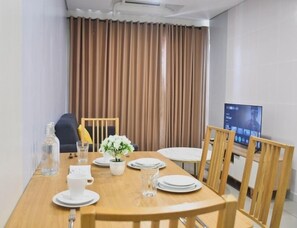 Un comedor con una mesa de madera dispuesta para cuatro, un televisor en la pared y una cortina de fondo.