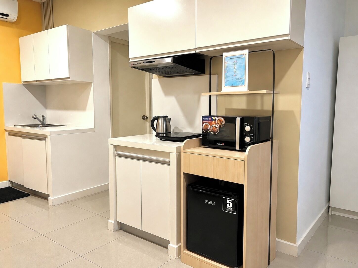 Una kitchenette compacta con microondas, hervidor de agua y un refrigerador pequeño.