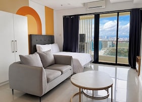 A modern hotel room with a bed, a sofa, a small table, and a city view through large windows.