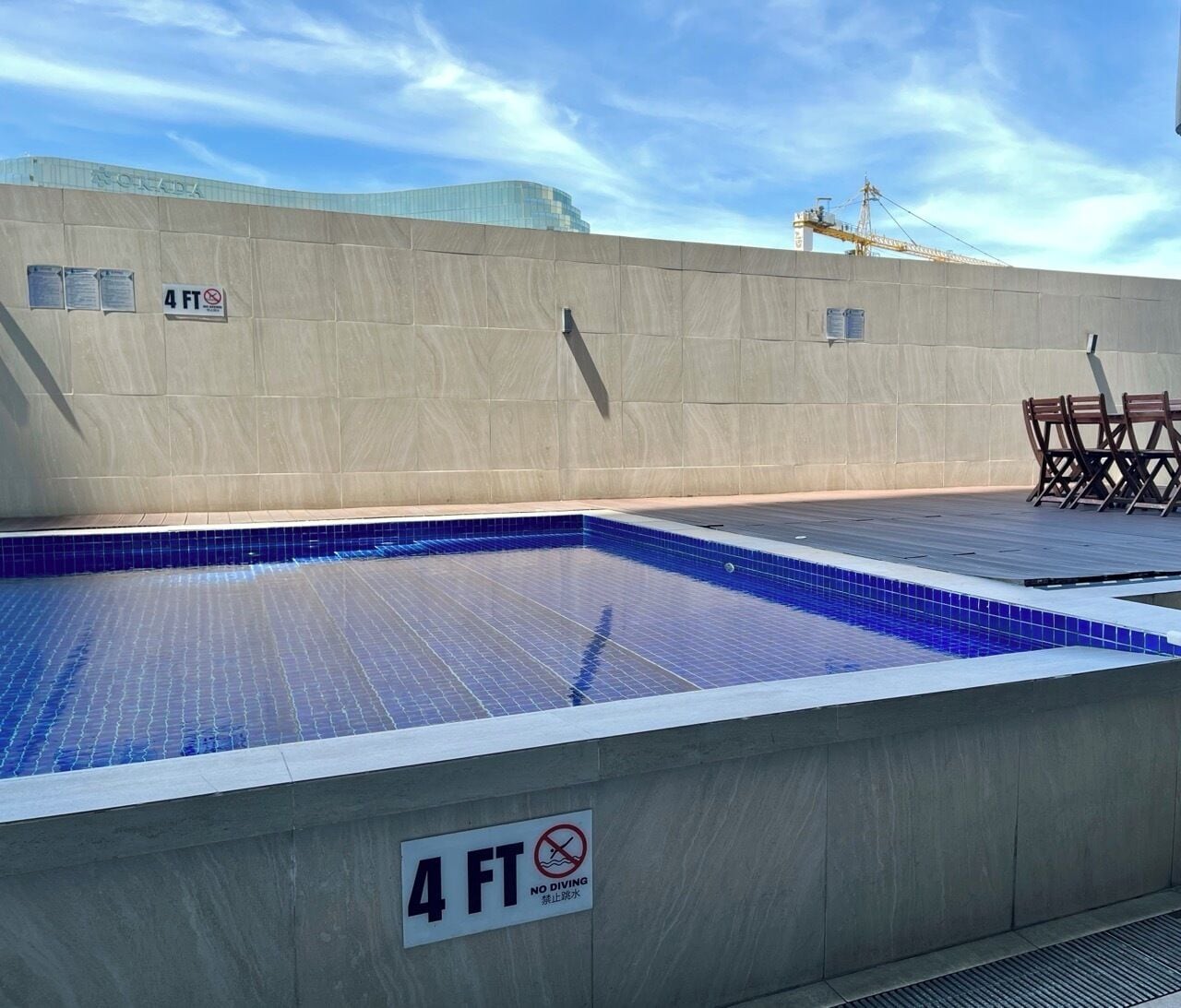 Una piscina en la azotea con un cartel de límite de profundidad de 1.2 metros, rodeada por un muro de concreto y un cielo despejado.