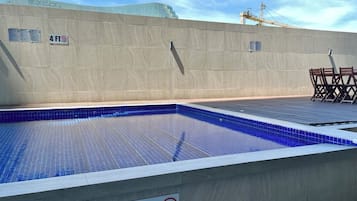 Una piscina en la azotea con un cartel de límite de profundidad de 1.2 metros, rodeada por un muro de concreto y un cielo despejado.