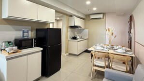 A modern kitchen with white cabinets, a black refrigerator, a microwave, and a dining area with a table set for two. - Sapphire Seaview Park (Parañaque)