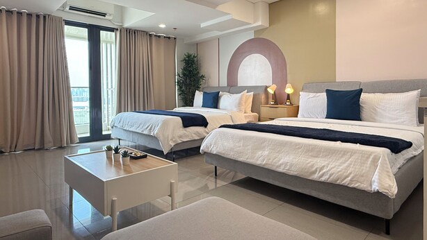 A modern hotel room with two beds, a small table, and a view of the outdoors. - Sapphire Seaview Park (Parañaque)