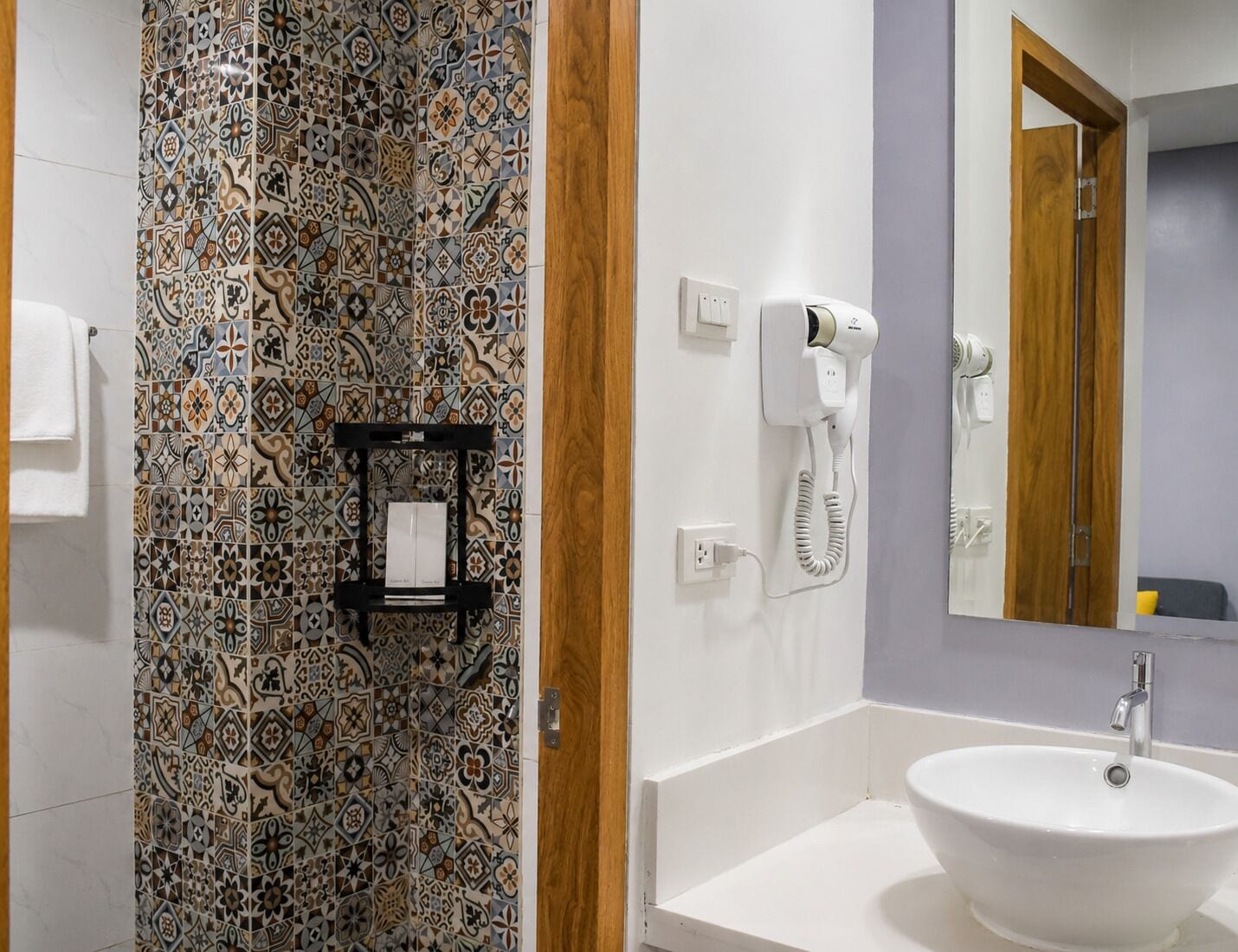 A bathroom with a patterned tile wall, a white sink, and a hairdryer on the wall.