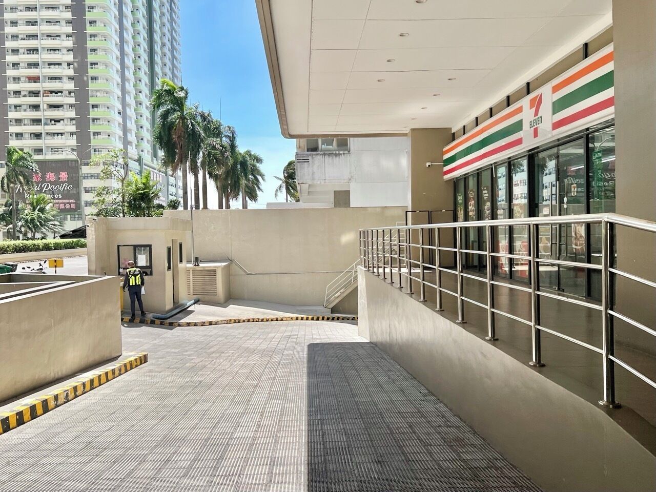 A 7-Eleven convenience store with a modern design, located in a high-rise building with a view of palm trees and other buildings.