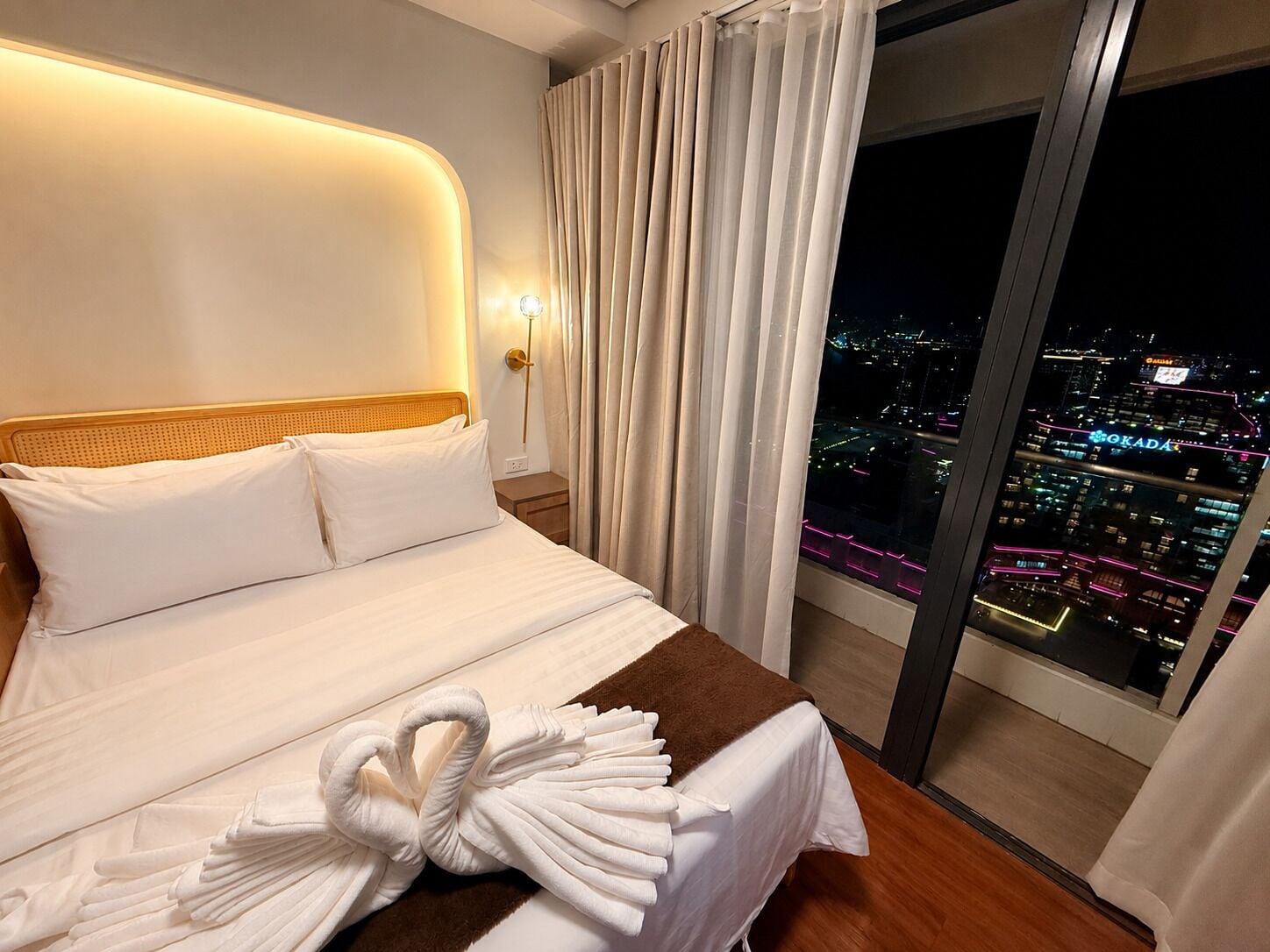 A hotel room with a bed, a night view of the city, and a cityscape visible through the window.