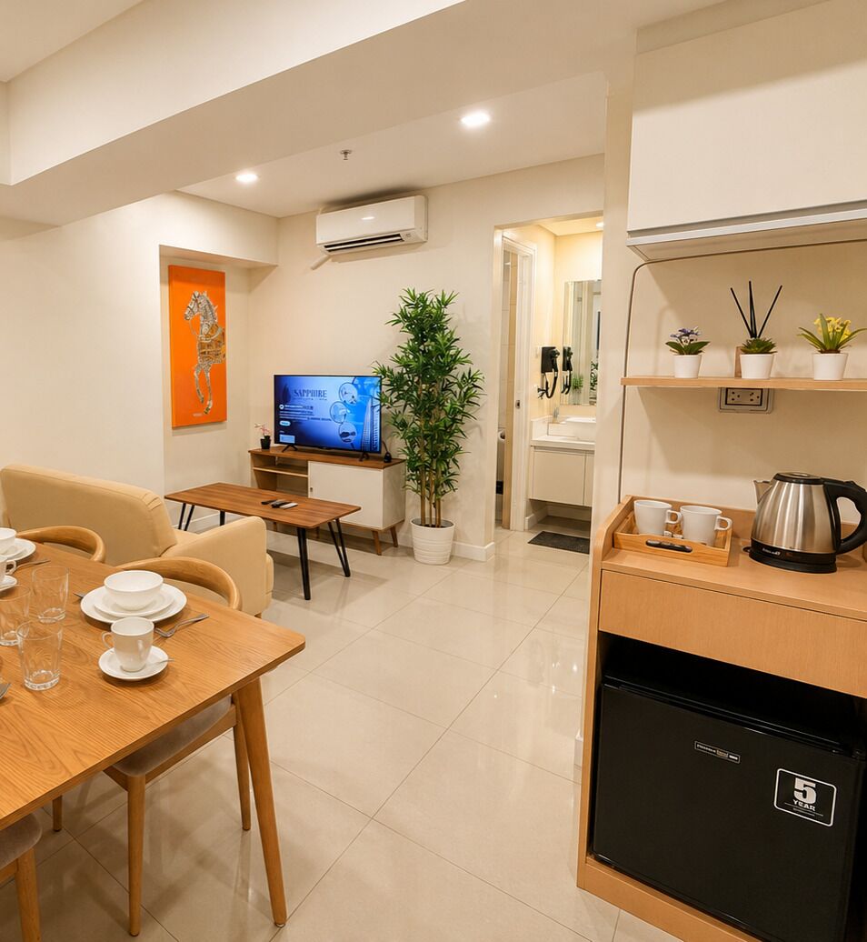 Een moderne hotelkamer met een zithoek, een televisie, een kamerplant en een kitchenette.