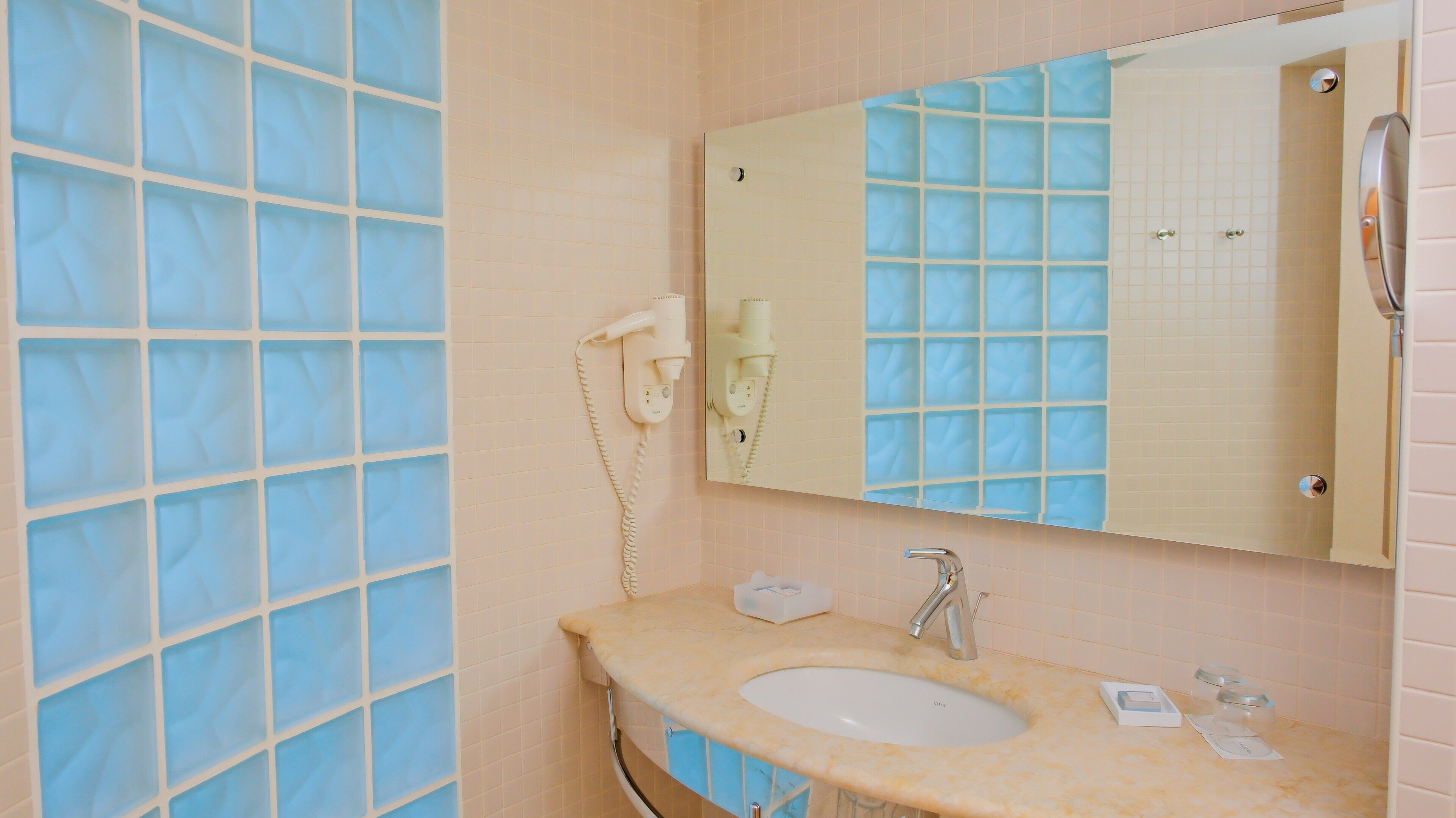 A bathroom with a sink, mirror, and a hairdryer on the wall.