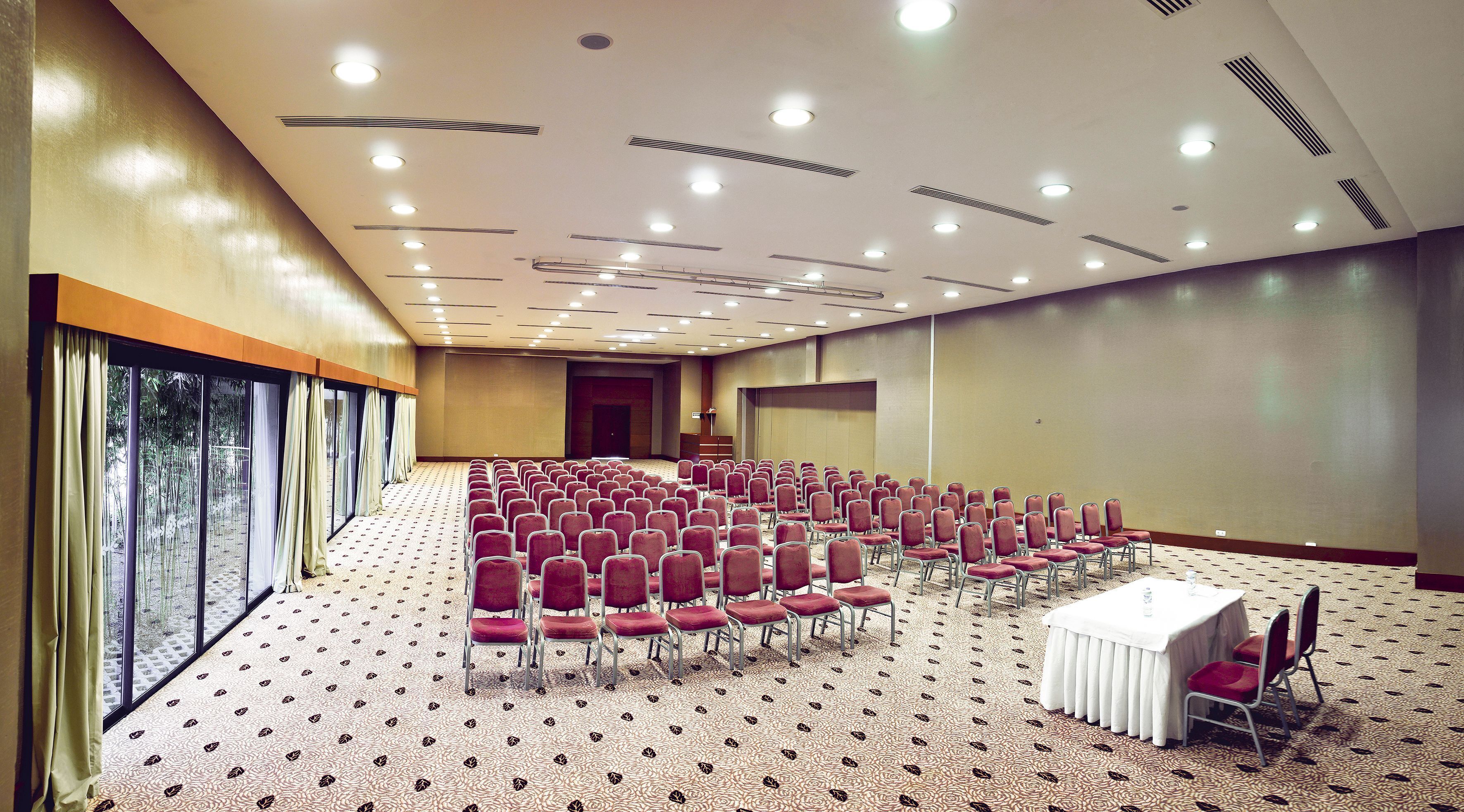 A conference room with rows of red chairs, a white table, and large windows with curtains.