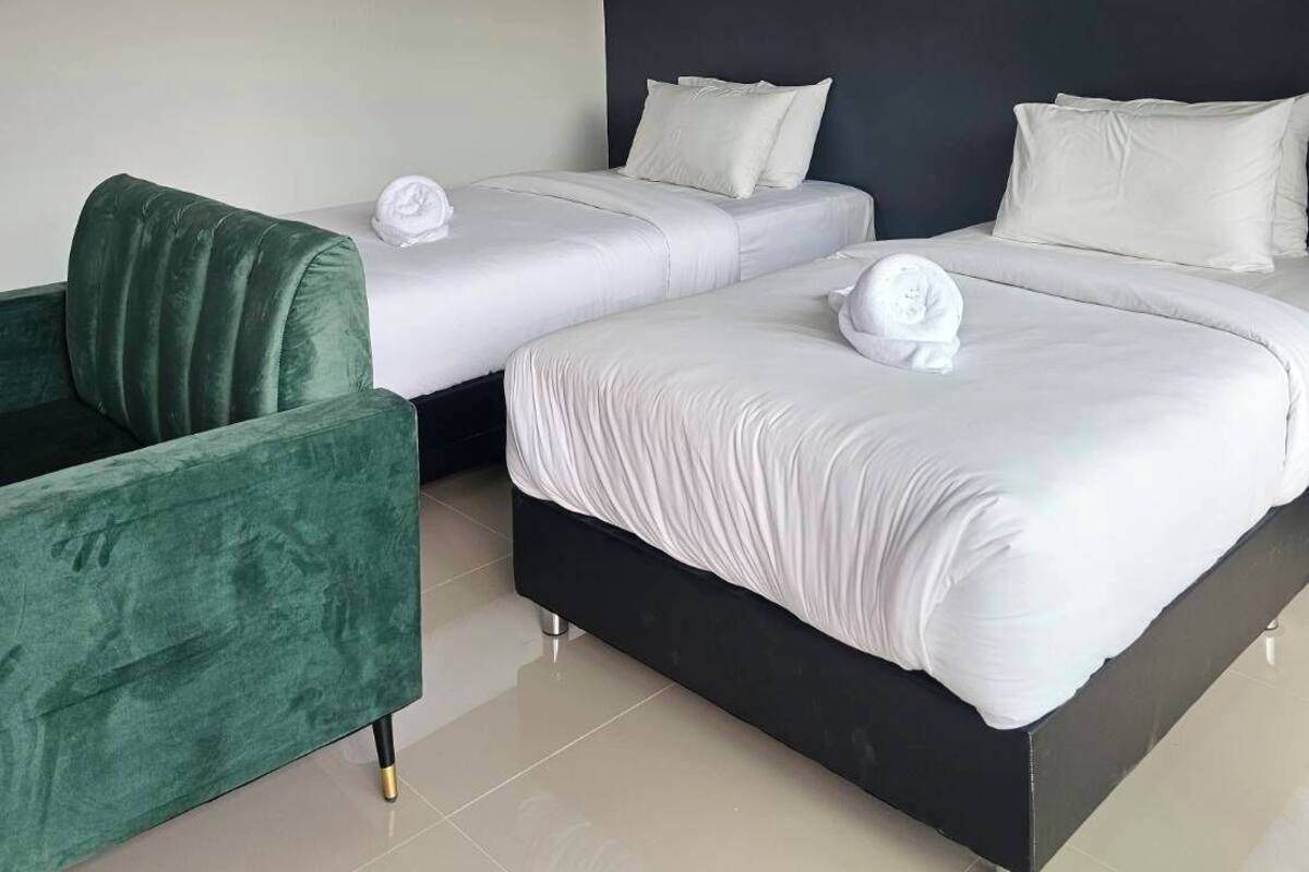 Ein modernes Hotelzimmer mit zwei Betten, einem grünen Sessel und einer wandmontierten Klimaanlage.