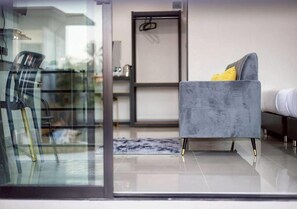 A modern living room with a grey sofa, a glass partition, and a view of the outside. - Hillside Premium Hotel (Surat Thani)