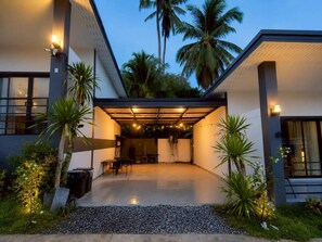 A modern house with a covered patio, palm trees, and a gravel driveway.