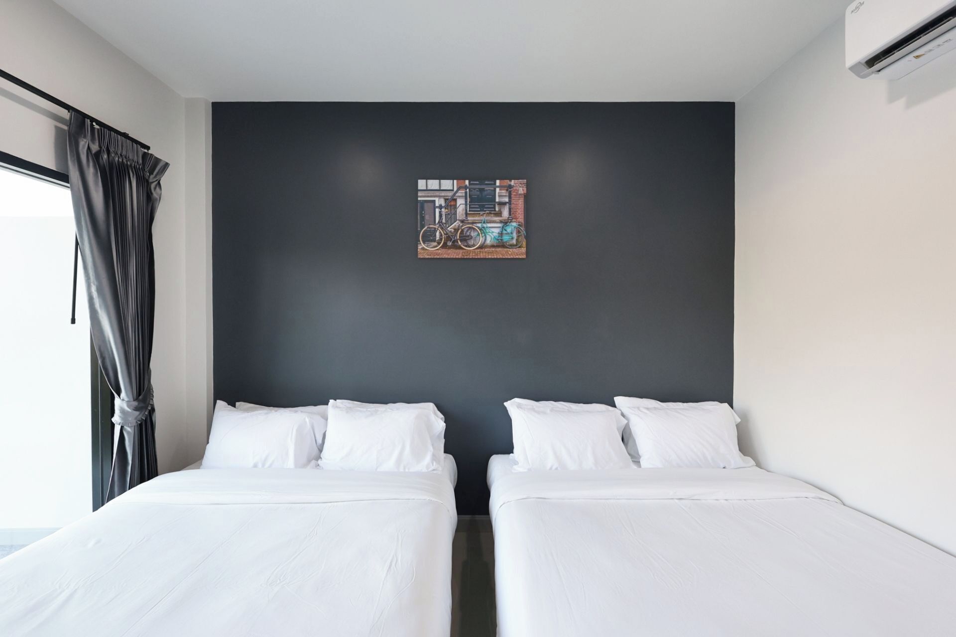 A hotel room with two beds, a dark wall, and a painting of bicycles.