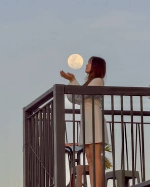Una persona de pie en un balcón con barandilla, mirando la luna.