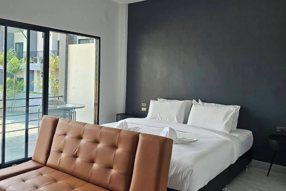 Ein modernes Schlafzimmer mit einem großen Bett, einer braunen Ledersofa und Blick ins Freie durch große Fenster.