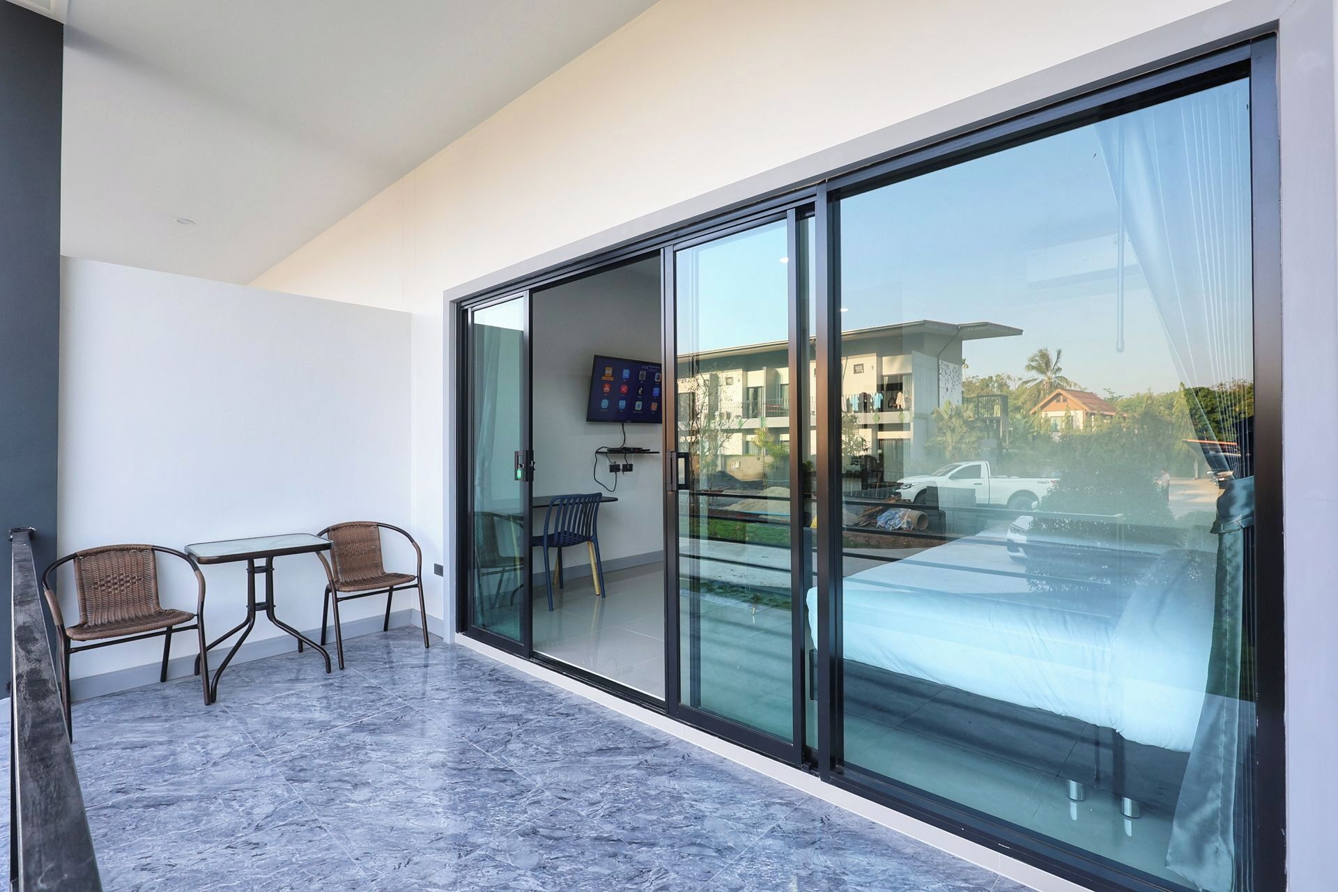 A balcony with a glass door, a small table, two wicker chairs, and a TV mounted on the wall.