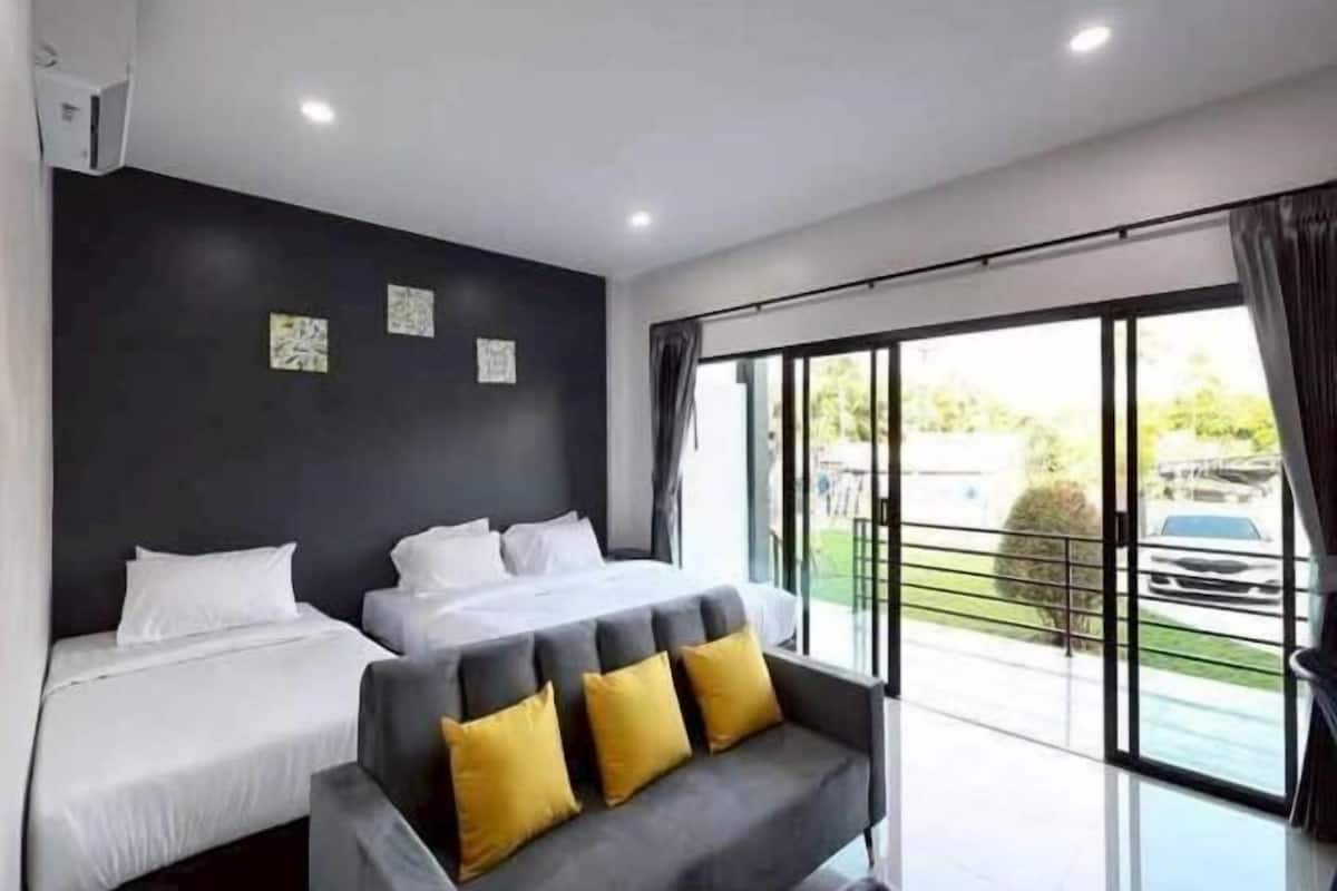 Een moderne hotelkamer met twee bedden, een bank en een grote schuifglazen deur naar buiten.