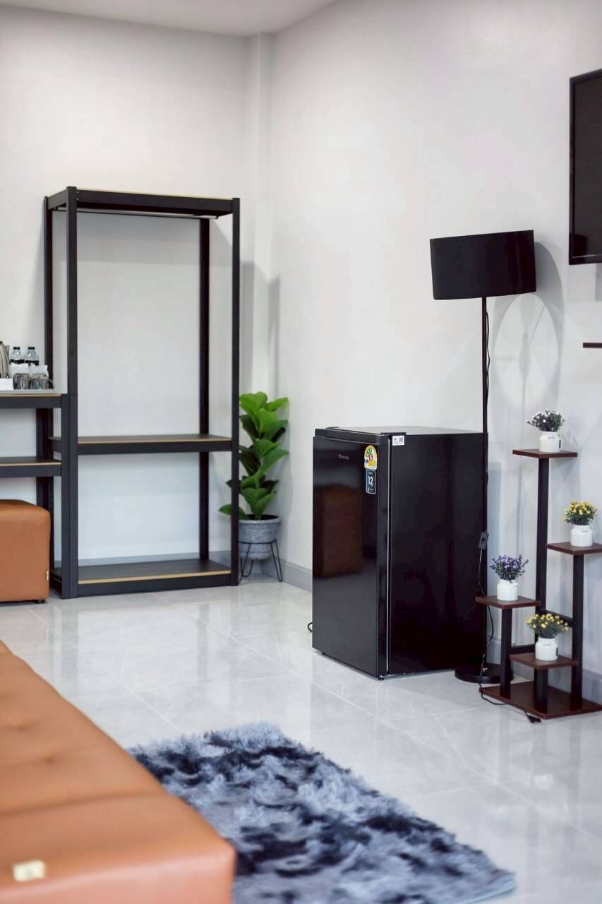 Een moderne woonkamer met een bank, een zwarte koelkast, een flatscreen televisie, een plant en een klein schap met decoratieve spullen.