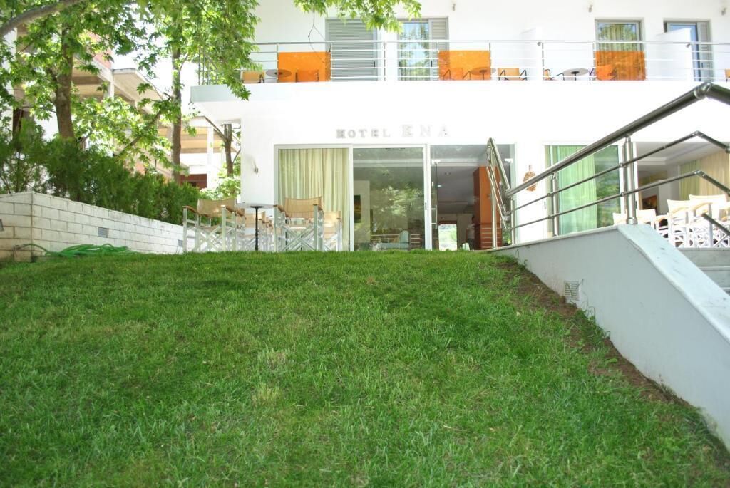 Un hotel con un patio delantero cubierto de césped, una escalera que conduce a la entrada y un balcón con cojines naranjas.