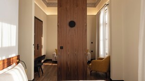 A hotel room with a neatly made bed, a wooden door, and a view of the hallway. - Bouquet Luxury Rooms (Chania)