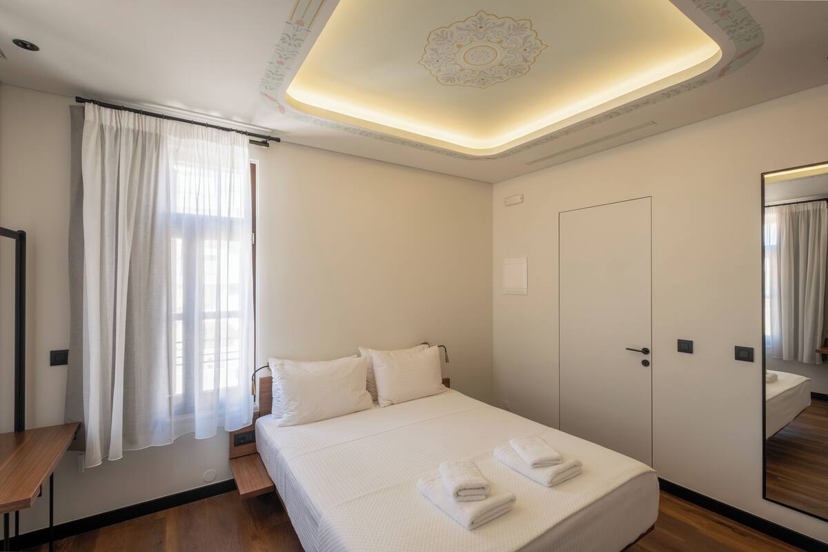Quarto de hotel com uma cama bem arrumada, um espelho grande e soalho de madeira.