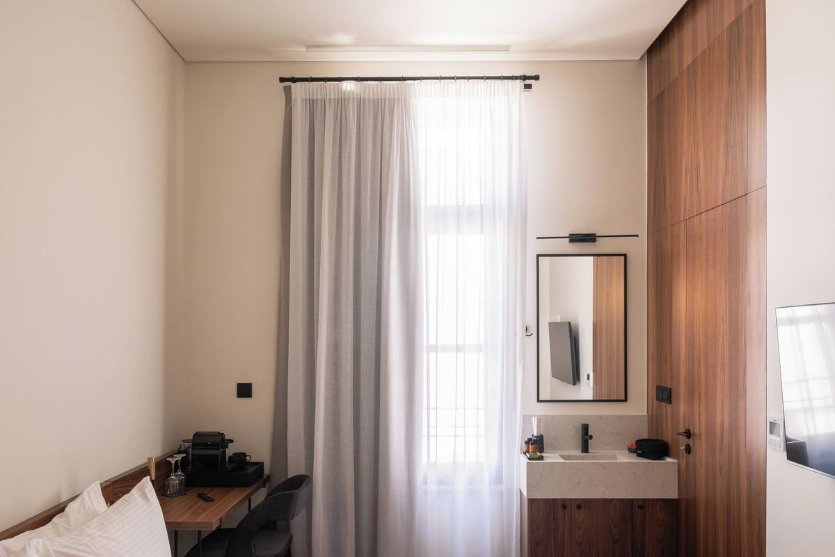 Quarto de hotel com cama, escrivaninha, espelho e guarda-roupa de madeira.