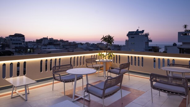 A rooftop terrace with seating and tables, overlooking a cityscape at dusk. - Bouquet Luxury Rooms (Chania)