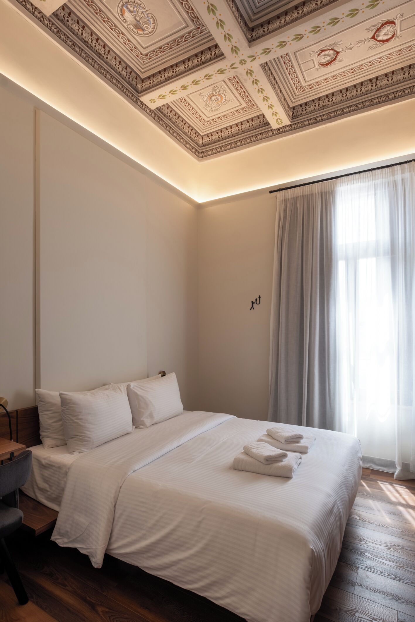 A hotel room with a large bed, a desk, and a ceiling with intricate patterns.