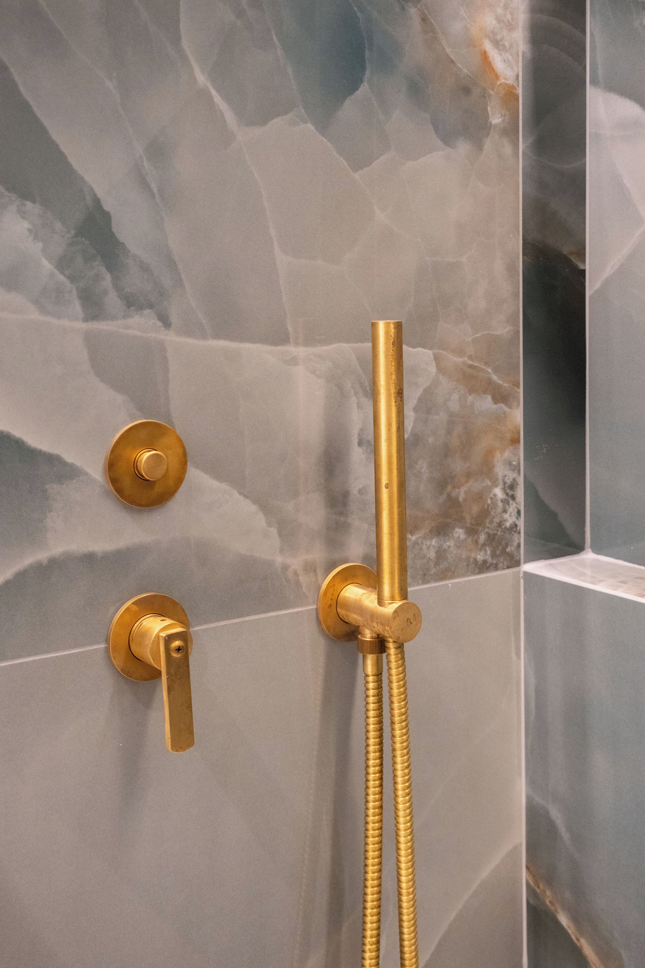 A shower with a gold faucet and hose, set against a marble wall.