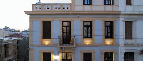 A multi-story building with a balcony on the second floor, a gated entrance, and a visible address number.