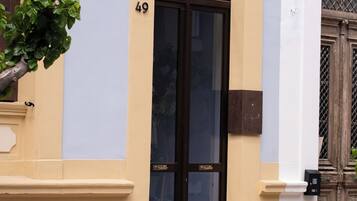 Un edificio con una puerta negra grande, paredes beige y azul claro, y una base de piedra.