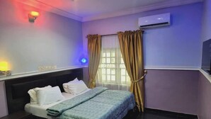 A hotel room with a bed, bedside table, air conditioning unit, and curtains. - New Eastern Comfort Hotel Umuahia (Umuahia)