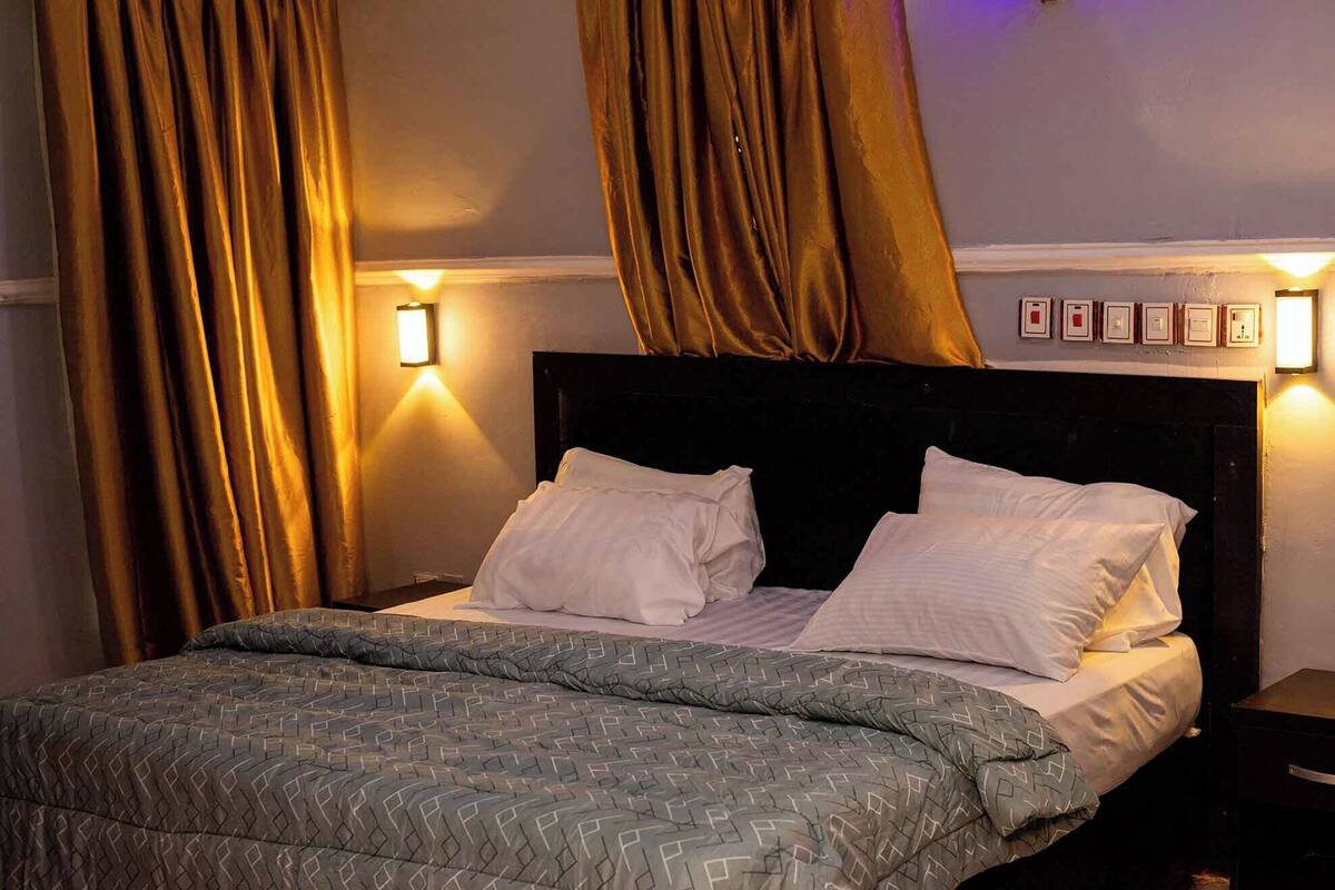 A neatly made bed with a patterned bedspread, two pillows, and a headboard with wall-mounted lights.